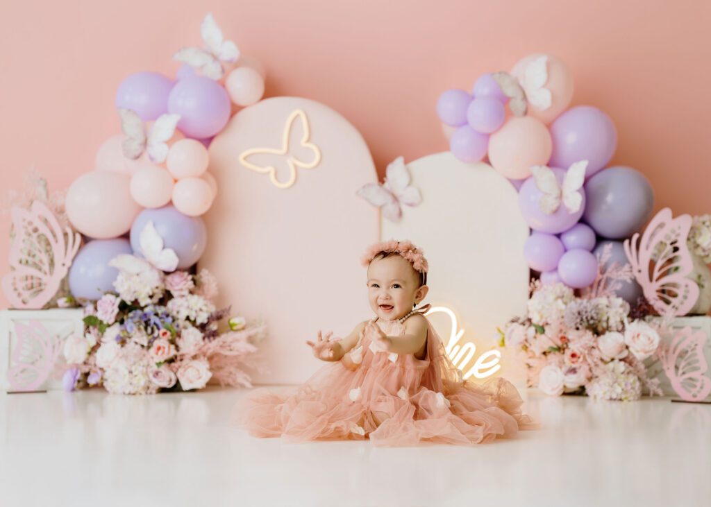 Butterfly-themed first birthday photoshoot with pastel balloons and floral decor.