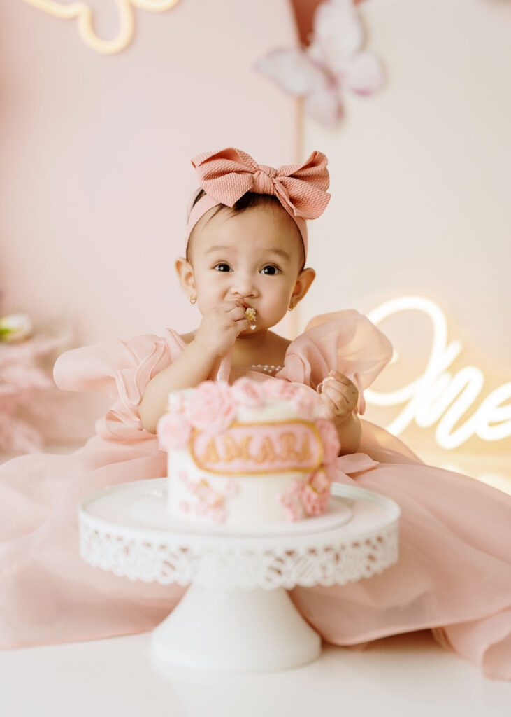 Baby girl celebrating her first birthday with a pink butterfly cake smash setup.
